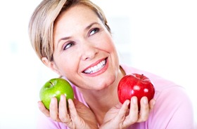 Smiling woman with dental implants in Torrington and apples