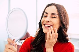 Happy patient using mirror to admire her dental implant restorations