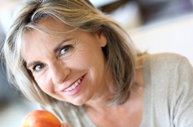 Woman holding apple, enjoying benefits of All-on-4 implants