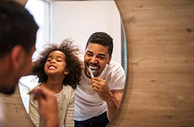 Father and daughter prevent dental emergencies by brushing teeth