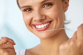 Smiling woman preparing to floss as part of her oral hygiene routine