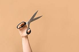 Hand holding pair of scissors against neutral background