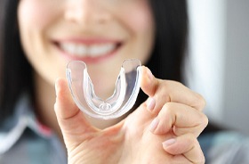 Woman holding clear mouthguard for teeth grinding prevention