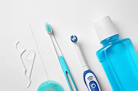 Floss, toothbrushes, and mouthwash lined up against white background
