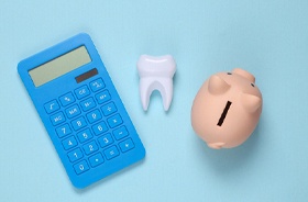 Calculator, tooth model, and piggy bank against blue background