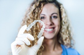 smiling dental professional holding Invisalign® aligner in foreground