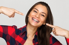 Happy woman with dark hair pointing at her traditional braces