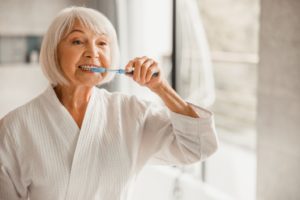 older woman at home brushing teeth during COVID-19