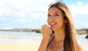 Woman on beach, applying lip balm
