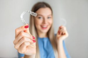 Smiling young woman holding Invisalign aligner