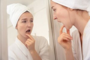 Woman inspecting her teeth and gums in bathroom mirror 